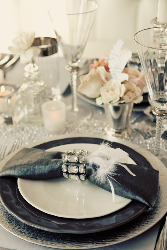 a glam NYE tablescape with silver chargers and black plates, black napkins, pastel blooms and pillar candles
