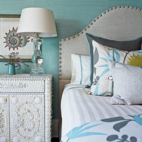 Sea-themed wall art and white sea shells that are covering a bedside table complete light blue wall color to make an interesting impression.