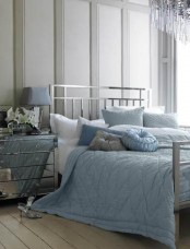 a grey bedroom with a silver finish bed, a mirror nightstand and blue and grey bedding