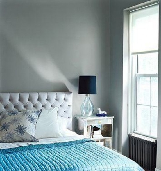 a light grey bedroom, a grey upholstered bed and a turquoise blanket plus navy lamps