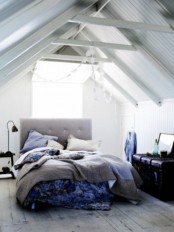 a light grey and creamy attic bedroom with a grey upholstered bed and grey and blue bedding