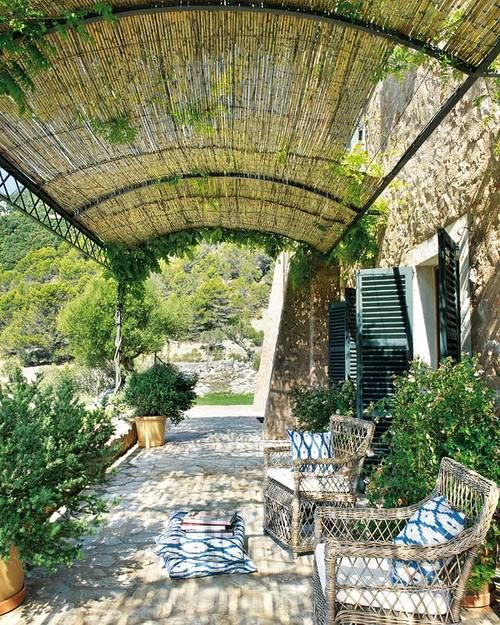 a relaxed Spanish patio with wicker chairs, potted greenery and blue printed pillows