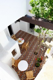 a boho patio with a mosaic floor, wooden furniture, potted blooms and greenery and a pizza stove