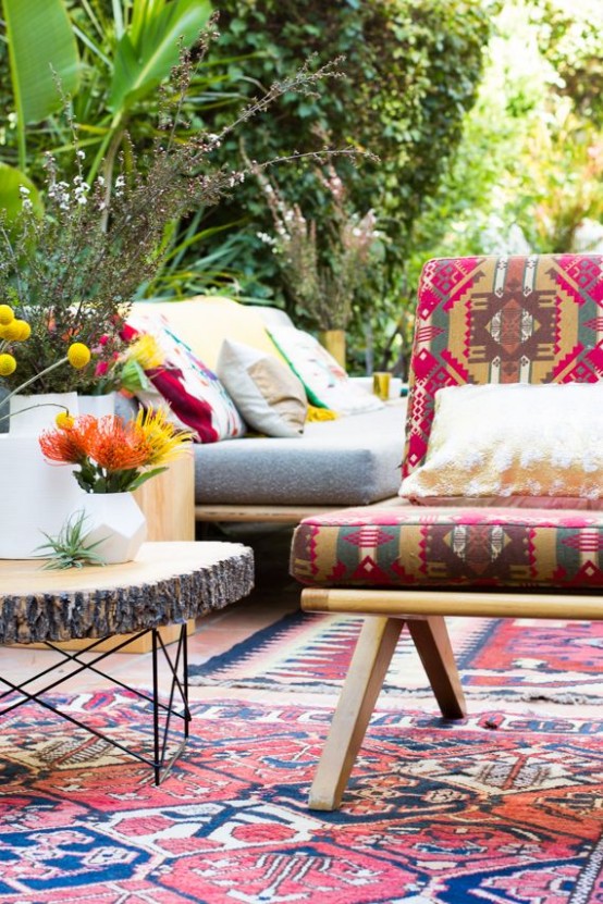 a bright boho patio with colorful rugs, furniture, pillows, a wooden slice coffee table and bright blooms
