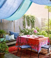 a colorful boho patio with a blue canopy, bright textiles and printed pillows, forged furniture