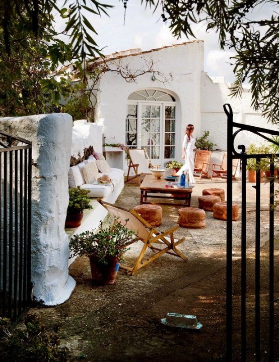 a boho patio in white with leather ottomans, folding furniture, potted greenery and blooms