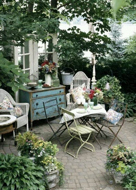 a relaxed patio in neutrals and pastels, with forged and wicker furniture and potted greenery and blooms