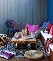 a super bright boho patio with a built-in bench, a rough wooden table on casters and super bright printed textiles, pillows and rugs