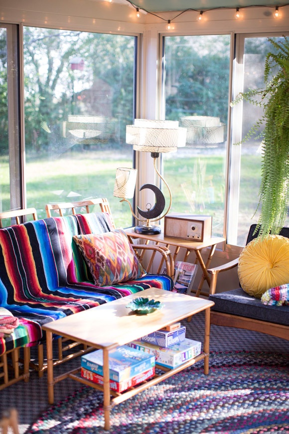 A colorful boho and mid century sunroom with a cool view, with furniture with bright textiles, pillows, rugs and some pretty potted plants is a cozy and cool space