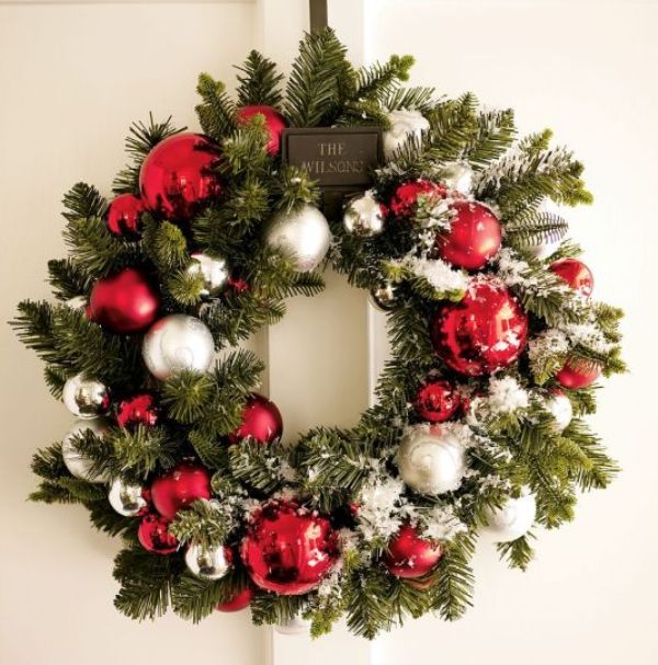 To decorate an evergreen wreath in a stylish way hang ornaments as if on a tree, grouping by color.