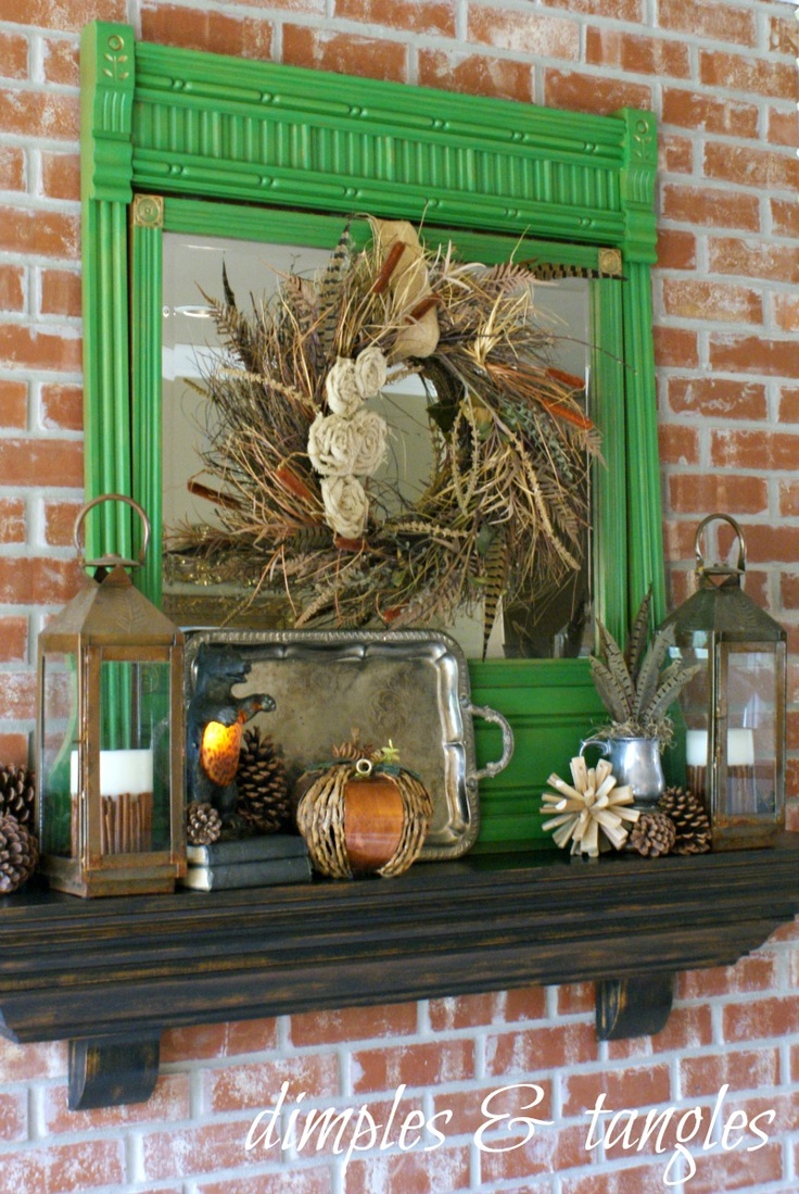 A quirky fall mantel with pinecones, pumpkins, candle lanterns, a mirror and feathers for a boho touch