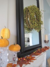 simple fall mantel decor with a mirror with a greenery wreath, fall leaves and acorns, faux pumpkins and candles