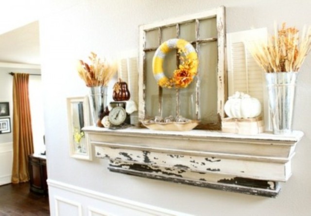A rustic fall mantel decorated with wheat and leaves, faux pumpkins and a fabric wreath hanging on a vintage window frame