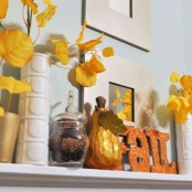 a yellow and orange fall mantel with yellow fall leaves, pinecones in glass jars and a faux pumpkin and glitter letters