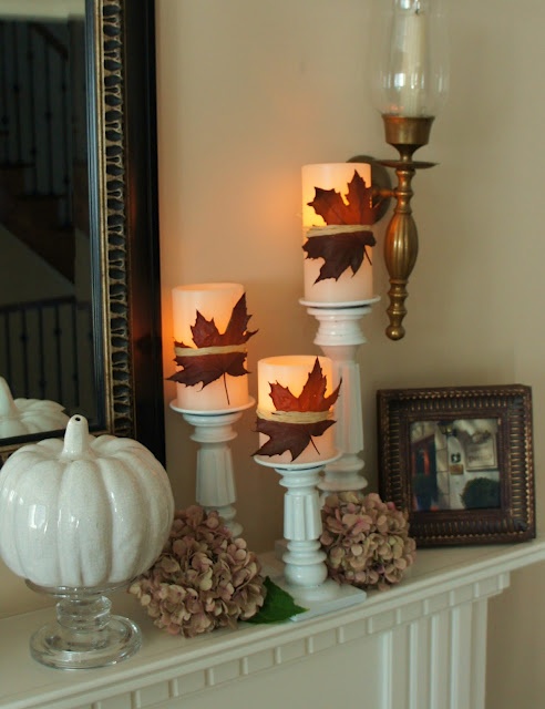 a simple fall mantel with a faux pumpkin, dried hydrangeas, candles with fall leaves attached in white candleholders