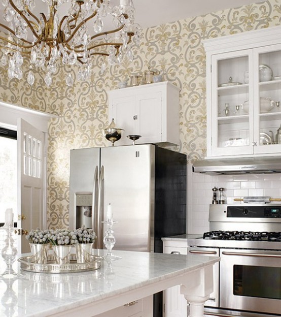 a retro glam kitchen with wallpaper walls, white cabinetry, a white marble countertop and a glam brass and crystal chandelier