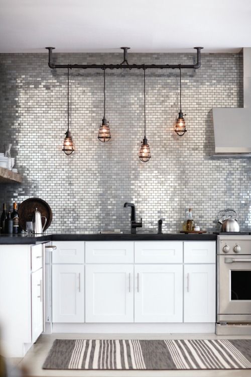 A modern kitchen with glam touches   white furniture, black countertops, a shiny silver tile backsplash and pendant lamps