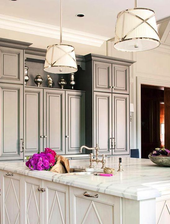 an old Hollywood glam kitchen with grey cabinetry, a white kitchen island with a marble countertop and chic pendant lamps