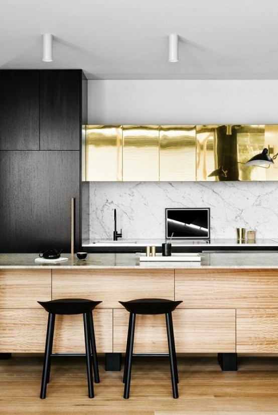 a modern glam kitchen with black and shiny gold cabinets, a wooden kitchen island with white marble countertops