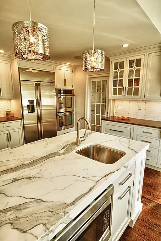 a vintage glam kitchen with neutral cabinetry, marble countertops, shiny touches and cool metal pendant lamps