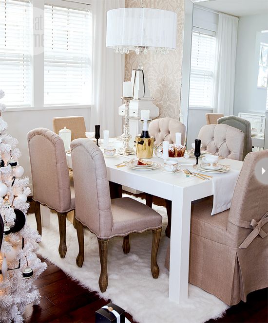 a vintage glam neutral dining room with gold patterned walls, a large floor mirror, a white table and tan chairs, some chic lamps and candleholders