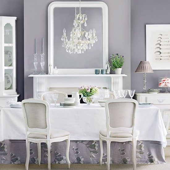 a refined neutral dining room with grey walls, a white fireplace, a long table and refined chairs, a crystal chandelier and beautiful lamps