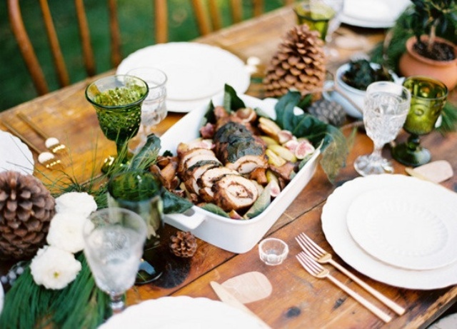 A cozy Christmas tablescape with white blooms, greenery, pinecones, green glasses and white porcelain is a lovely solution