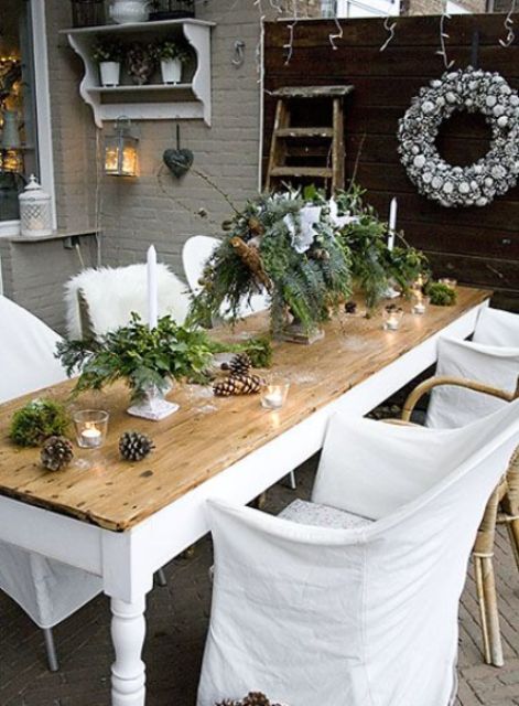 an outdoor Christmas tablescape with a greenery centerpiece with ornaments and pinecones, candles and pinecones on the table is cool