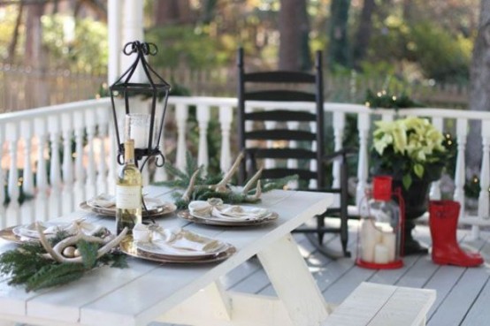 a simple outdoor Christmas tablescape with evergreens, antlers, ornaments and neutral porcelain is a cool idea