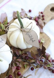 a cutting board with cherries, greenery and white pumpkins with tags for a Thanksgiving centerpiece