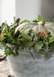 a galvanized bucket with greenery and berries and a large heirloom pumpkin for a rustic touch in your space