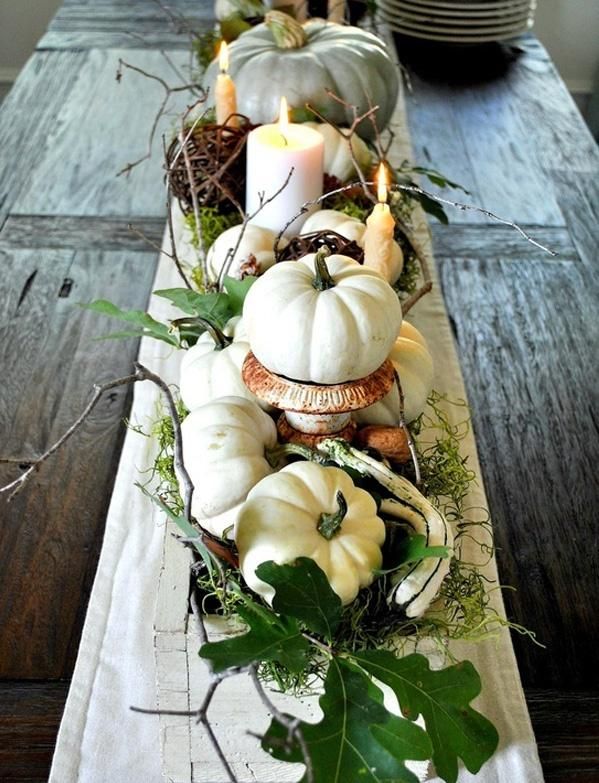 A Thanksgiving table runner of pumpkins on stands, greenery, antlers, twigs and candles