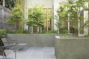 a small townhouse garden with stone tiles, concrete flower boxes, minimalist furniture and greenery and trees growing