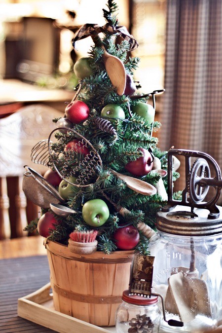a fun mini Christmas tree in a wooden basket, with apples, wooden spoons, metal kitchen accessories