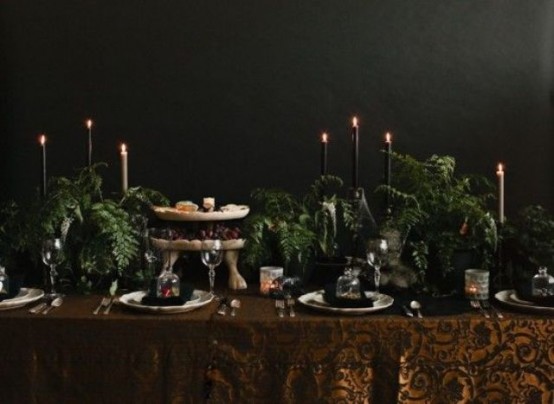 a Halloween tablescape with a rust printed tablecloth, black and white candles, lots of greenery and refined plates and glasses