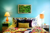 a colorful bedroom with turquoise walls, a bed with colorful bedding, mismatching nightstands, table lamps and a bold artwork and bright pillows