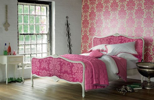 a bright bedroom with a pink printed wallpaper wall, chic vintage white furniture, pink and white bedding and metallic decorations for a more refined look