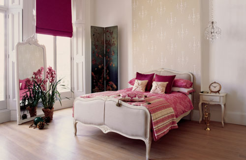 a neutral vintage bedroom done with bright textiles, with a bright printed bedding, a fuchsia curtain and some blooms and a bright space divider
