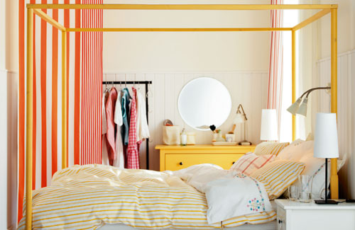 a neutral bedroom with a bold yellow dresser, a yellow canopy bed, a bold striped space divider, a bright bedding set