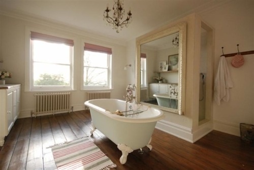 A beige and creamy bathroom, a rich colored wooden floor and a large mirror plus windows