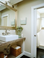 a beige and white bathroom with a rustic vanity surface and a gilded frame mirror