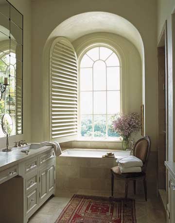 A creamy and beige vintage inspired bathroom with an arched window and a chic vanity