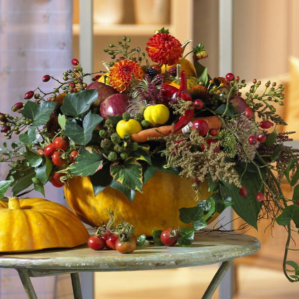 A super bold and all natural Thanksgiving centerpiece with a bold pumpkin as a vase, lots of fresh veggies, berries, greenery and some brigth blooms is gorgeous