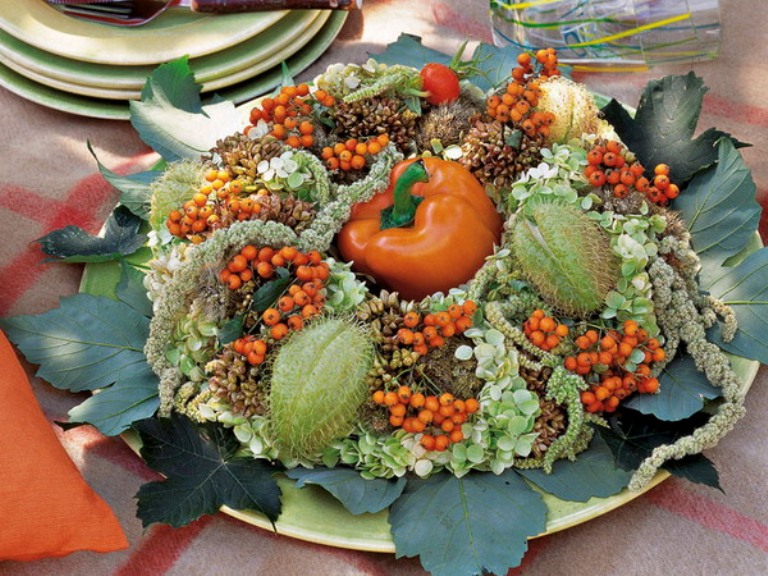 A pretty Thanksgiving centerpiece of a plate with greenery, berries, fruits and an orange pepper in the center is a creative all natural idea