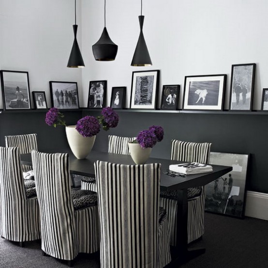 a catchy black and white dining room with black paneling that doubles as ledges for the gallery wall, a black table and striped chairs, black pendant lamps