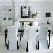 a vintage black and white dining space with printed wallpaper, a fireplace, a black table and white chairs, a crystal chandeliet