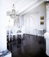 a vintage dining space with whitewashed walls and a ceiling, a black floor and a white dinign set, a crystal chandelier