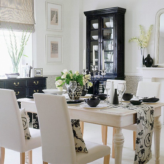 a black and white Scandinavian dining room with a black sideboard and a buffet, a white vintage table and creamy chairs, printed textiles