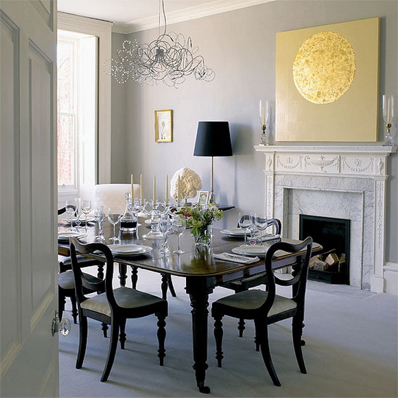 A neutral dining room with a non working fireplace, an elegant black dining set and a crystal chandelier