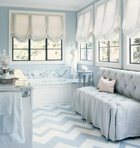 a refined bathroom done with powder blue, with a tufted sofa, a chevron floor and a marble tub